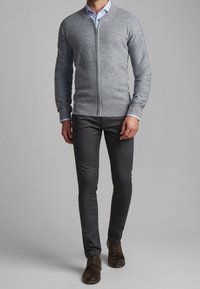 Cardigan gris en maille avec fermeture éclair à l'avant, encolure ronde et poignets côtelés, associé à un pantalon slim noir et des chaussures à lacets marron.