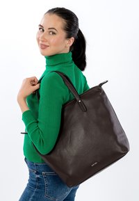 Ruda odinė pirkinių rankinė su akmenukų tekstūra, turinti dvi tvirtas rankenas ir minimalias metalines detales. Rankinė nešiojama ant peties.