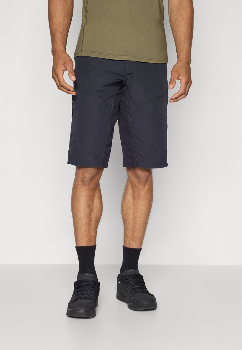 Shorts bleu marine avec une texture lisse, dotés de coutures angulaires et de poches latérales. Associés à des baskets noires et des chaussettes sombres.