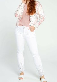 Giacca di jeans bianca con motivo floreale, maglione di lana rosa chiaro e pantaloni bianchi con pizzo. Texture morbide, dettagli con bottoni e sottili decorazioni.