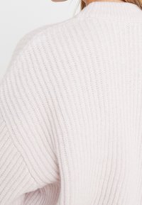 Jasnoróżowy sweter z dzianiny o prążkowanej teksturze i luźnym kroju. Posiada okrągły dekolt i opadające ramiona, co  tworzy przytulny wygląd.