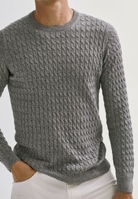 Pull gris en maille avec un motif torsadé texturé, col rond et manches longues. Le tissu semble doux et légèrement extensible.