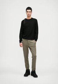 Sort tekstureret sweater, khaki bukser og sorte sneakers. Sweateren har rund hals og tætsiddende manchetter. Bukserne er tapered med en glat overflade.