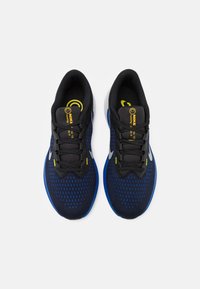 Scarpe da ginnastica blu e nere con parte superiore in rete, colletto imbottito e suola intermedia bianca. Presentano un marchio giallo e lacci neri.