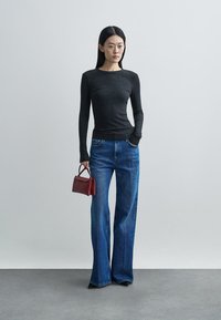 Μαύρο ριμπ μπλουζάκι με μακριά μανίκια συνδυασμένο με μπλε τζιν παντελόνι φαρδιάς γραμμής και μικρή μπορντό τσάντα, πάνω σε ουδέτερο γκρι φόντο.