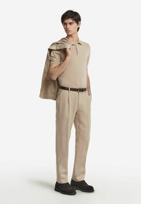 Beige polo skjorta i kombination med beige veckade byxor. Jacka slängd över axeln, brun läderbälte och mörkbruna mockaskor.