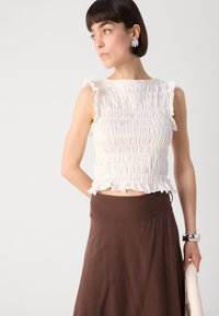 Crop top bianco con volant sul collo, abbinato a una lunga gonna marrone. Il top presenta un design testurizzato e una silhouette aderente.