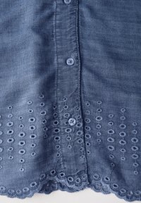 Denimskjorta i mörkblått med knäppning, som har broderade cirkulära mönster och scallopad fåll längs den nedre kanten.