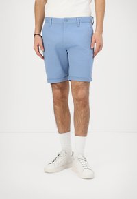 Pantalones cortos de algodón azules con dobladillos enrollados, cierre de botón, bolsillos frontales y una textura suave, combinados con zapatillas blancas y calcetines.