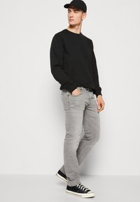 Fekete pulóver és szürke, slim fit farmer, fekete-fehér sportcipővel párosítva. Az öltözék laza stílusú, egyszerű textúrákkal.