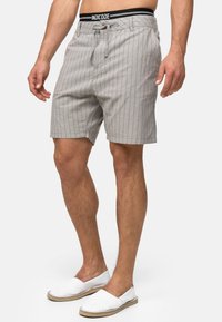 Grå stribede shorts med snøre i taljen og et sort mærket elastikbånd, suppleret med hvide slip-on sko med en jutesål.