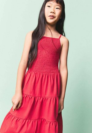 Robe en coton rouge avec un corsage smocké, des bretelles fines et une jupe à volants. Le tissu est lisse avec un léger éclat et semble léger.