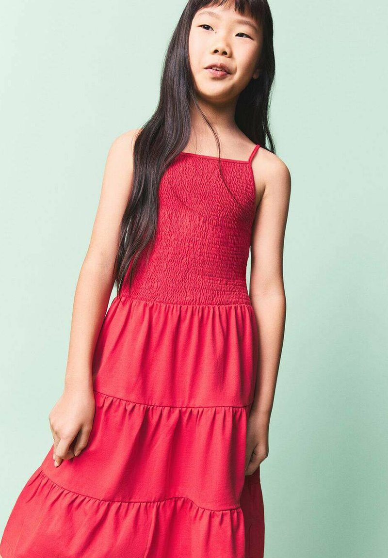 Robe en coton rouge avec un corsage smocké, des bretelles fines et une jupe à volants. Le tissu est lisse avec un léger éclat et semble léger.