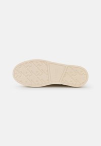 Suola di scarpa beige con battistrada decorato e logo impresso al centro, mostrata su uno sfondo bianco uniforme.