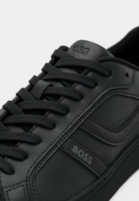 Baskets en cuir noir avec lacets noirs, couture détaillée et "BOSS" embossé sur le côté et la languette.