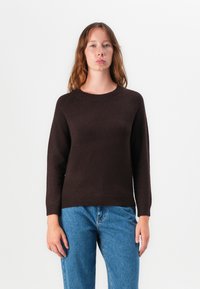 Mørkebrun strikkegenser med rund hals og raglanermer, kombinert med lyseblå jeans. Myk tekstur, enkelt design.