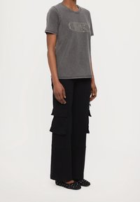 Camiseta gris de manga corta con cuello redondo y logo de strass, combinada con pantalones cargo negros con múltiples bolsillos y un corte relajado.