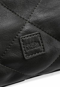 Zwarte leren tas met een doorgestikte textuur en contrasterende stiksels. Voorzien van een vierkante label met de tekst "FRED BRUDER" in reliëf.