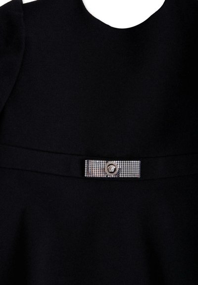 Czarna sukienka z gładkiego, teksturowanego materiału, okrągłym dekoltem oraz ozdobnym metalowym paskiem z kryształkami i detalem w postaci emblemu.