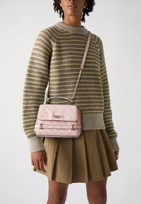 Borsa rosa realizzata in materiale texturizzato, con manico superiore, tracolla a catena e design con logo impresso, indossata sopra un maglione a righe e una gonna.