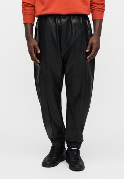 Černé jogger kalhoty z umělé kůže s bočními zipy, elastickými manžetami a panelovým designem. Doplněné černými teniskami.