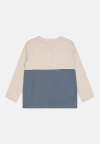 Langermet skjorte med en beige øverste del og en blå nederste del. Laget av mykt stoff, med en enkel rund hals og rett søm.