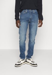 Blå denimjeans med smal passform och lätt urblekt look. Matchas med svart långärmad t-shirt och svart-vita sneakers.