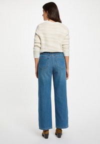 Jeans de denim azul de pierna ancha con una cintura alta, que cuentan con dos bolsillos traseros y un suéter de punto texturizado de color claro.