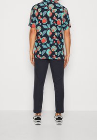 Lyhythihainen paita tummansinistä taustaa vasten, jossa on värikäs kukka- ja hedelmäkuvio. Yhdistetty tummansinisiin housuihin ja tennareihin.