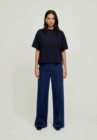 Námornícky krátky rukáv tričko s uvoľneným strihom, skombinované s širokými tmavomodrými džínsami. Hladká tkanina a minimalistický dizajn.