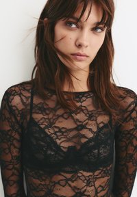 Fekete csipkéből készült, hosszú ujjú felső virágmintákkal, alatta egy hozzá illő bralette. Az anyag különleges, áttetsző, finom foltokkal.