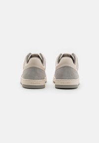 Sneaker beige con tacco grigio in suede, design arrotondato, tomaia testurizzata e marchio "COACH" ben visibile sulla suola.