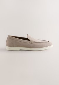 Mocassin en daim beige clair avec semelle blanche, profil bas et design sans lacets, vu de côté sur un fond clair uni.