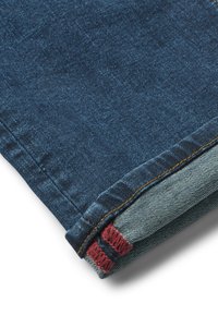Tissu en denim bleu foncé avec un ourlet replié, présentant des accents rouges et un dessous bleu clair contrasté. Couture détaillée visible le long du bord.