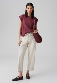 Bordeaux linnen top met korte mouwen, crèmekleurige wijde broek met trekkoord in de taille, en donkerbruine instappers met een gespdetail.