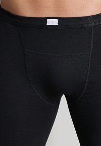 Black thermal leggings made of stretchy fabric; features a front pocket and elastic waistband with a small label at the back.