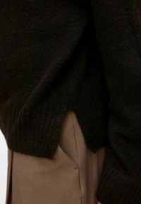 Czarny sweter z dzianiny o prążkowanej fakturze i bocznych rozcięciach, w połączeniu z brązowymi spodniami z boczną kieszenią i lekkiego materiału.