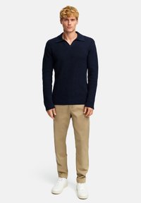 Pullover blu navy a maglia con scollo a V e colletto ampio, abbinato a pantaloni beige e sneakers bianche. Tessuto testurizzato con un motivo dettagliato.