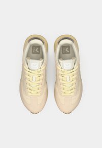 Μπεζ αθλητικά παπούτσια με υφή από δίχτυ και πάνελ από σουέντ, με κίτρινα κορδόνια και λεπτομέρειες, στρογγυλεμένη μύτη και επίπεδη σόλα από καουτσούκ.