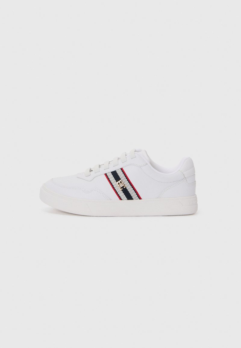 Sneaker bianco con tomaia texture, caratterizzata da strisce orizzontali nere e rosse, design con lacci e soletta in gomma piatta. Dettaglio del logo dorato presente.