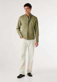 Camicia verde oliva a maniche lunghe realizzata in cotone, abbinata a jeans color crema e scarpe di pelle nere. Design semplice con una vestibilità rilassata.