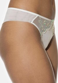 Array van witte doorschijnende string met bloemenborduursel in groenaccenten. Delicate kantafwerking langs de tailleband, die de lichte textuur benadrukt.