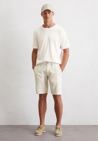 Light beige t-shirt paired with light striped shorts, and beige shoes. The outfit features a casual design with simple lines and a relaxed fit.