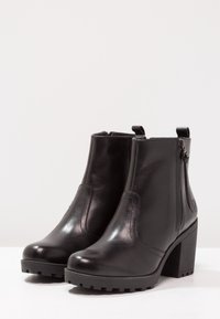 Bottes dcuir noir pour femme, finition lisse, bout rond, fermetures  glissire latrales, talon bloc chunky avec une semelle texture9e noire.