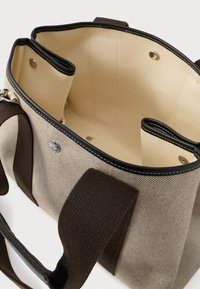 Plátěná taška v béžové barvě s hnědými akcenty, která nabízí prostorný interiér, patentní uzávěr a dvojité uši pro pohodlné nošení.