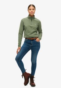 Groene fleece pullover met een halve rits, blauwe strakke jeans en bruine veterschoenen. Gelaagde stof met een subtiele logo-detail.