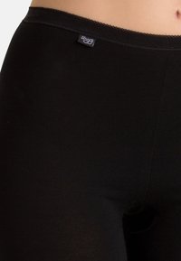 Schwarze Leggings aus weichem, dehnbarem Material mit glatter Oberfläche. Verfügt über einen zarten Spitzebesatz am Bund und ein kleines Logo-Tag.