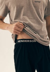 Szary bawełniany t-shirt w połączeniu z czarnymi spodniami; pasek w talii posiada napis "HENDERSON" w białym kolorze. Tkanina wydaje się miękka i ma luźny krój.