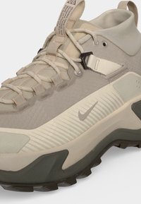 Μπεζ και ελιά πεζοπορικό παπούτσι Nike με υφή στην σόλα, χοντρά κορδόνια, υφασμάτινες θηλιές και μπρανταρισμένο λουράκι στην γλώσσα.