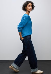 Blauwe satijnen lange mouwen top, donkere denim wijde broek met opgerolde mouwen en lichte sneakers. Eenvoudig ontwerp, gestructureerde stofafwerking.